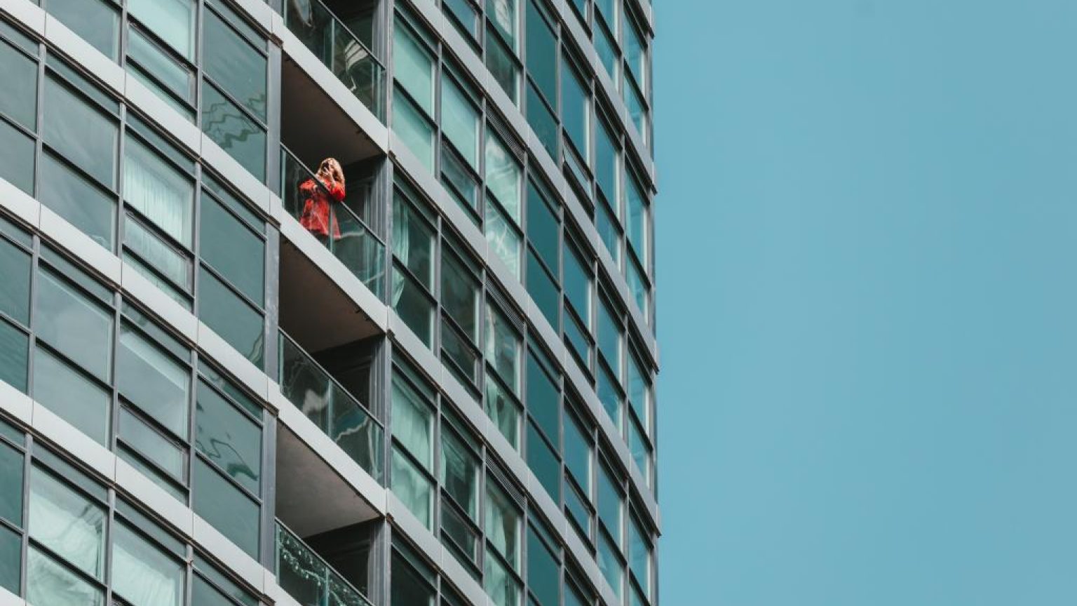 A woman in a red jacket inspects her phone on a balcony 1024x683