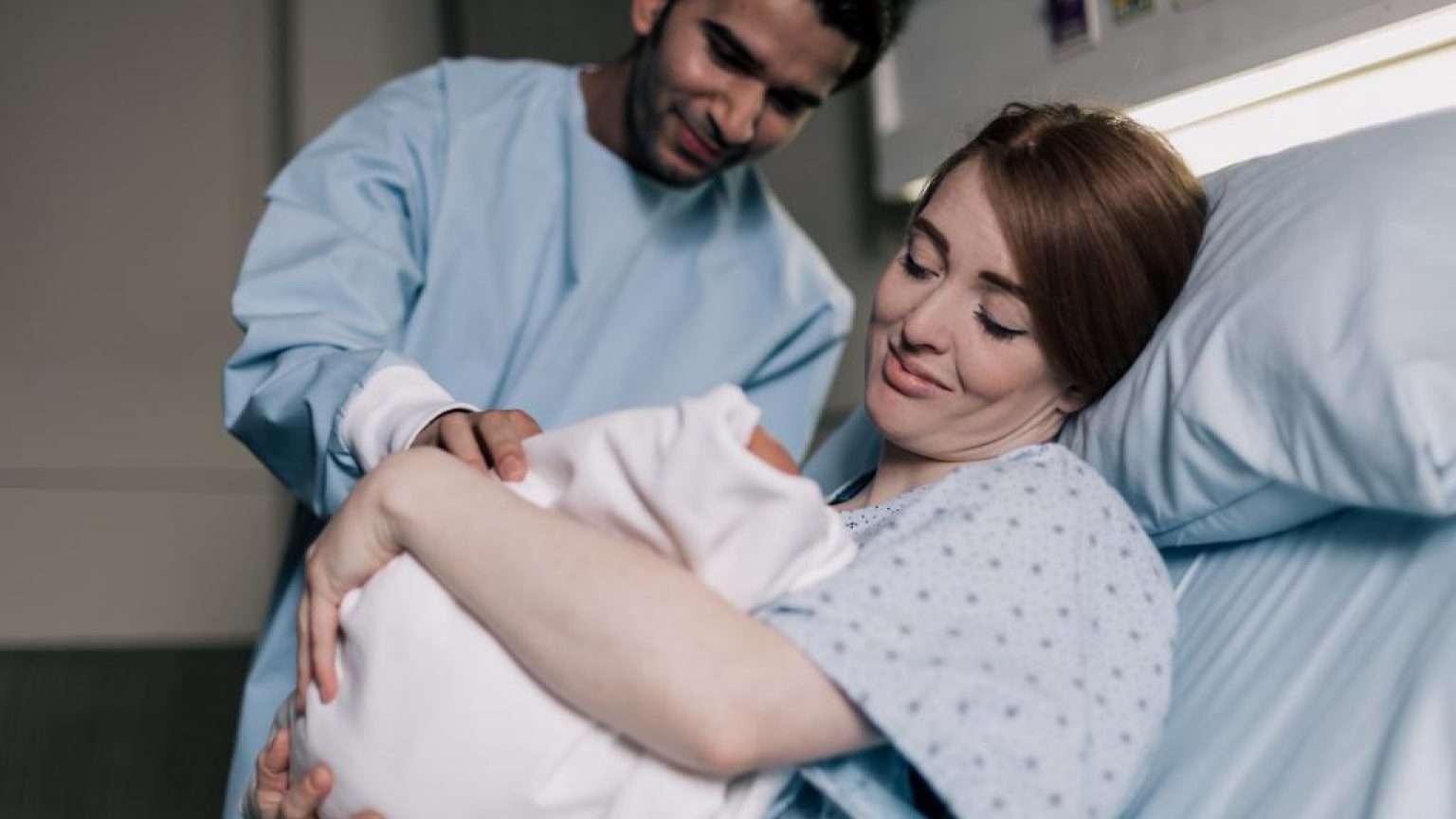 Mother and father smiling down on their newborn baby 1024x683